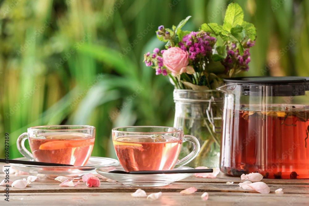 Flowers, teapot and cups with floral tea on table against blurred background