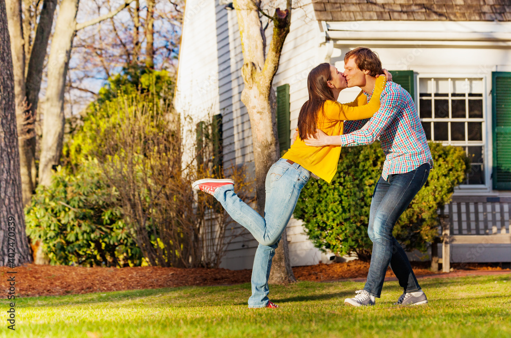 Dancing couple outside in the park standing on one leg kissing and having fun view from side