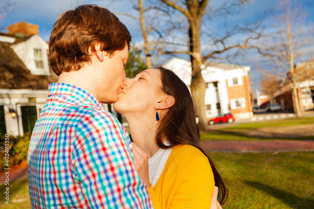 Young happy couple kiss close portrait stand in public park profile view