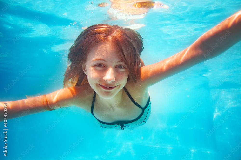 Nice friendly close portrait of the girl stretch hand, smile and swim underwater in the pool