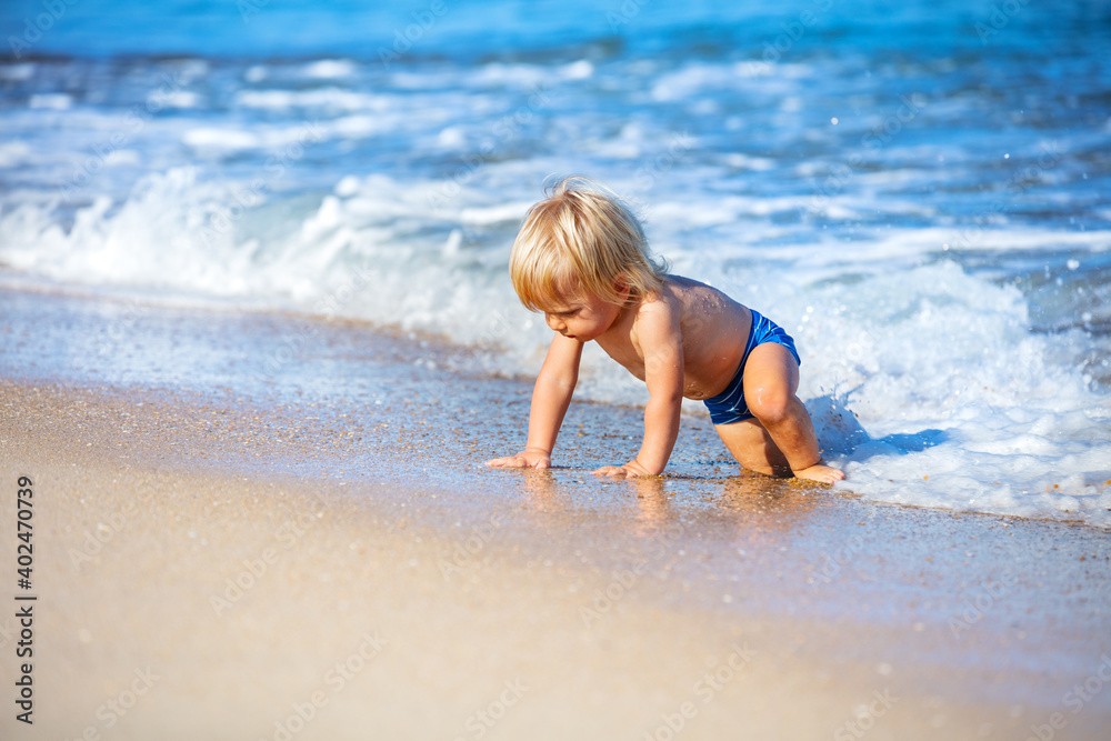 Happy little toddler play crawling running from waves in the sea towards the beach