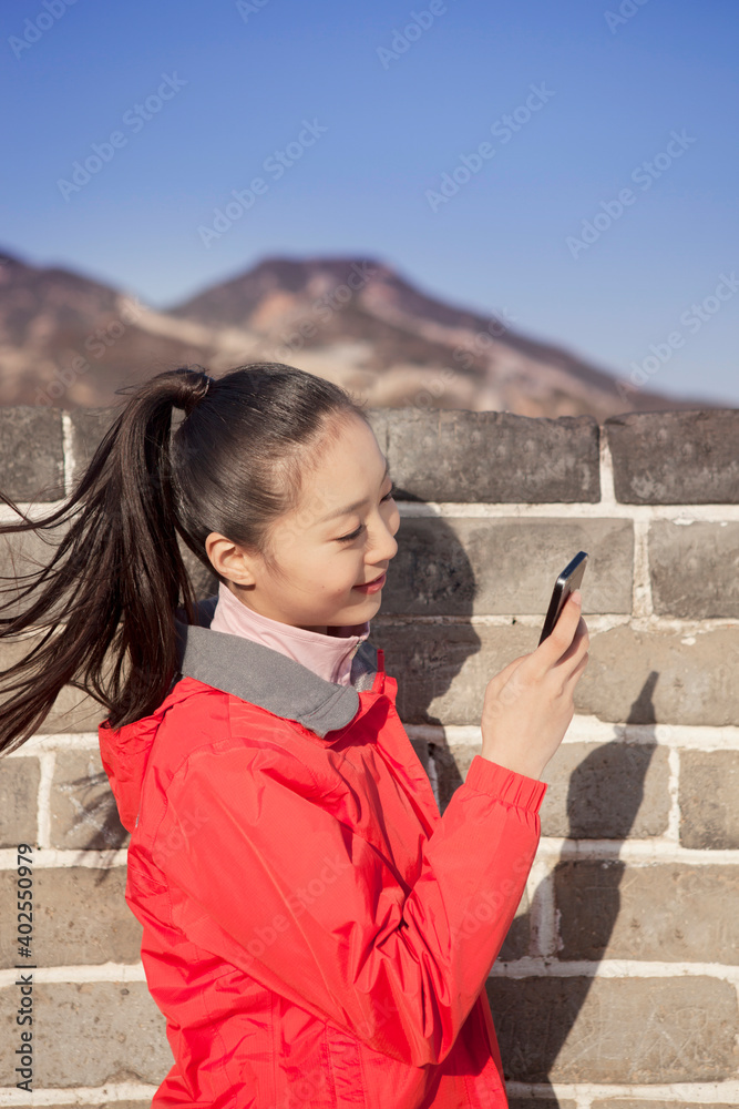 一名年轻女子在长城旅游中使用手机