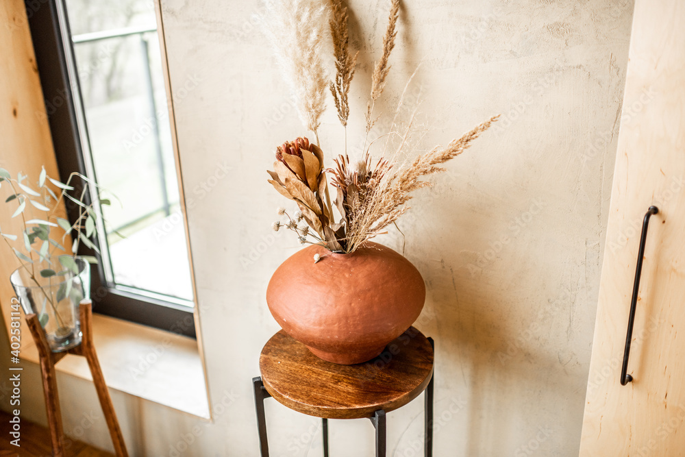 Composition of dried flowers in a clay vase on a beige wall background. Bouquet of pampas grass, cor