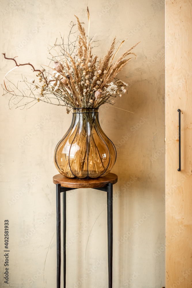 Composition of a dried herbs in a glass vase on a beige wall background