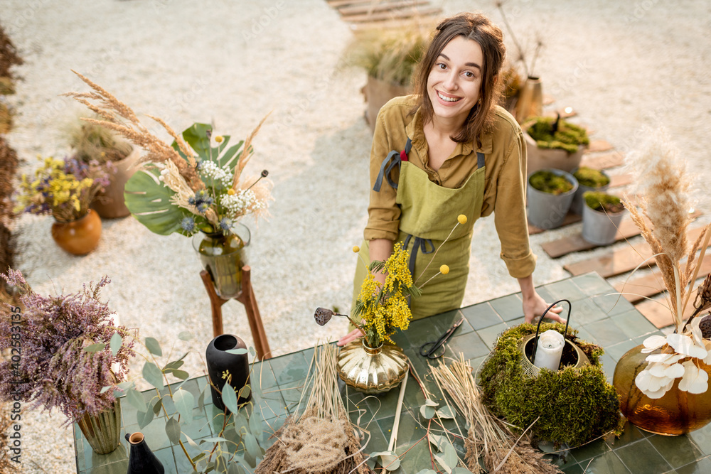 Portrait of a cheerful woman making compositions of dried and fresh flowers and herbs at the worksho