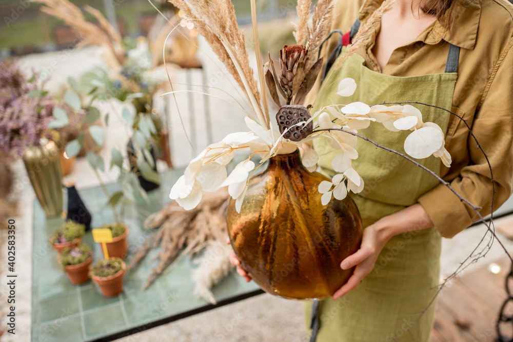 Florist holding composition of dried herbs in a glass vase outdoors