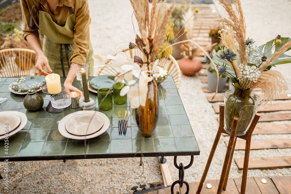 Young female lighting candles while decorating dinning table in natural Boho style in green tones ou