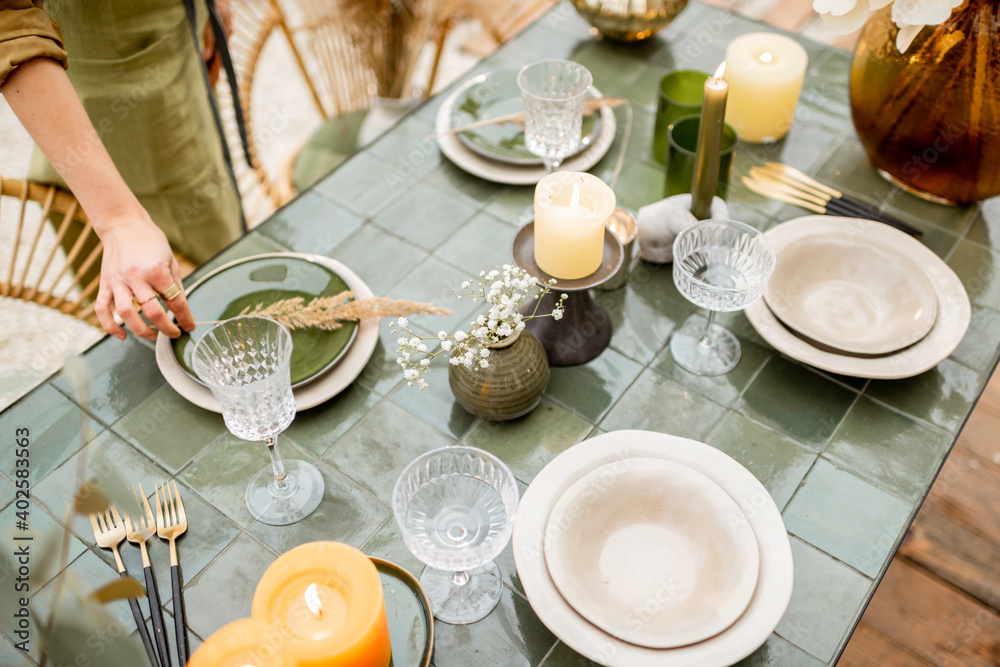 Young female putting herbs on a plates, decorating dinning table in natural Boho style in green tone