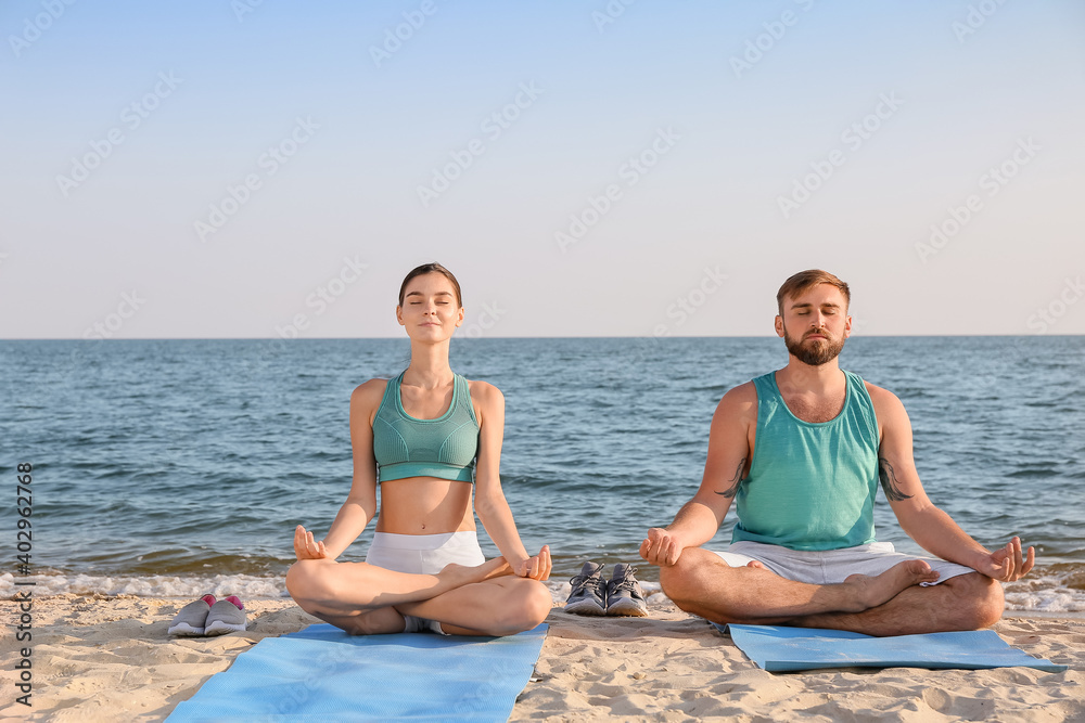 Sporty young couple practicing yoga on sea beach