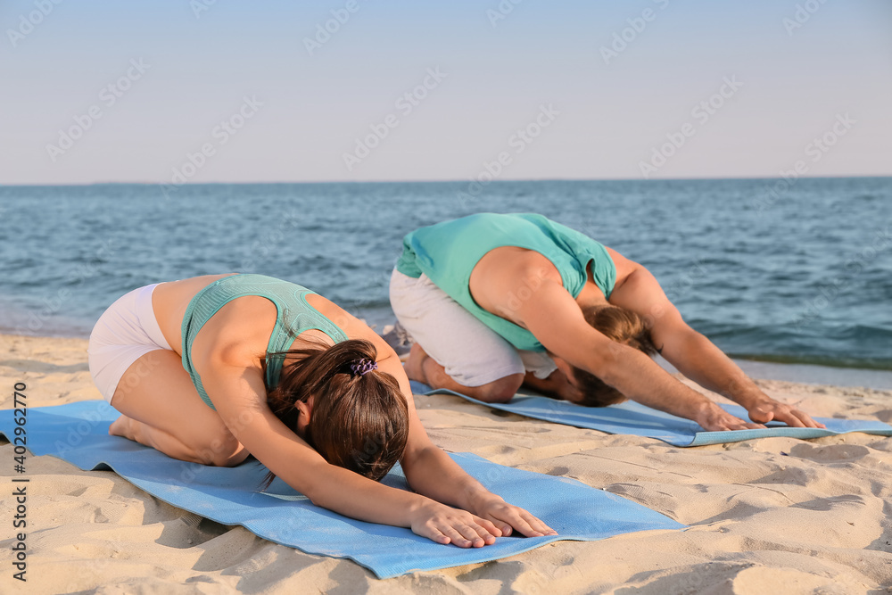 Sporty young couple practicing yoga on sea beach