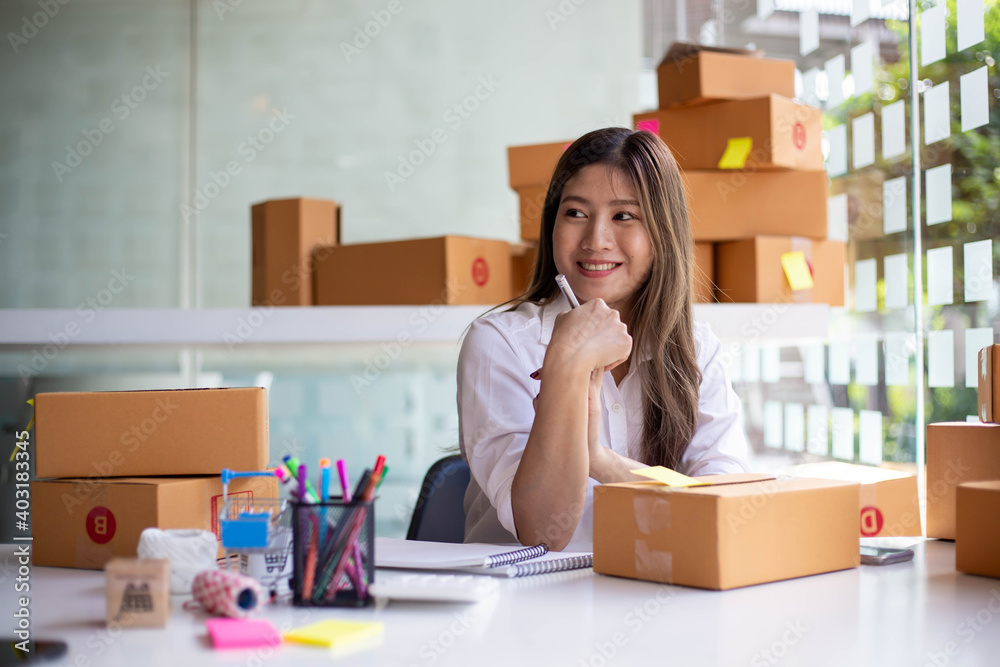 An Asian owner holds a package in a brown box, ready for delivery to a customer who orders online. A