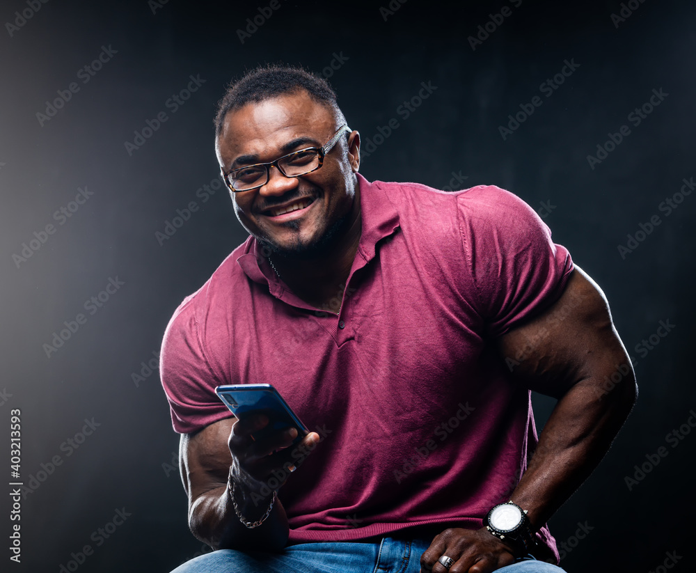 Smiling cheerful young black man poses with phone in hands over black background. African american i