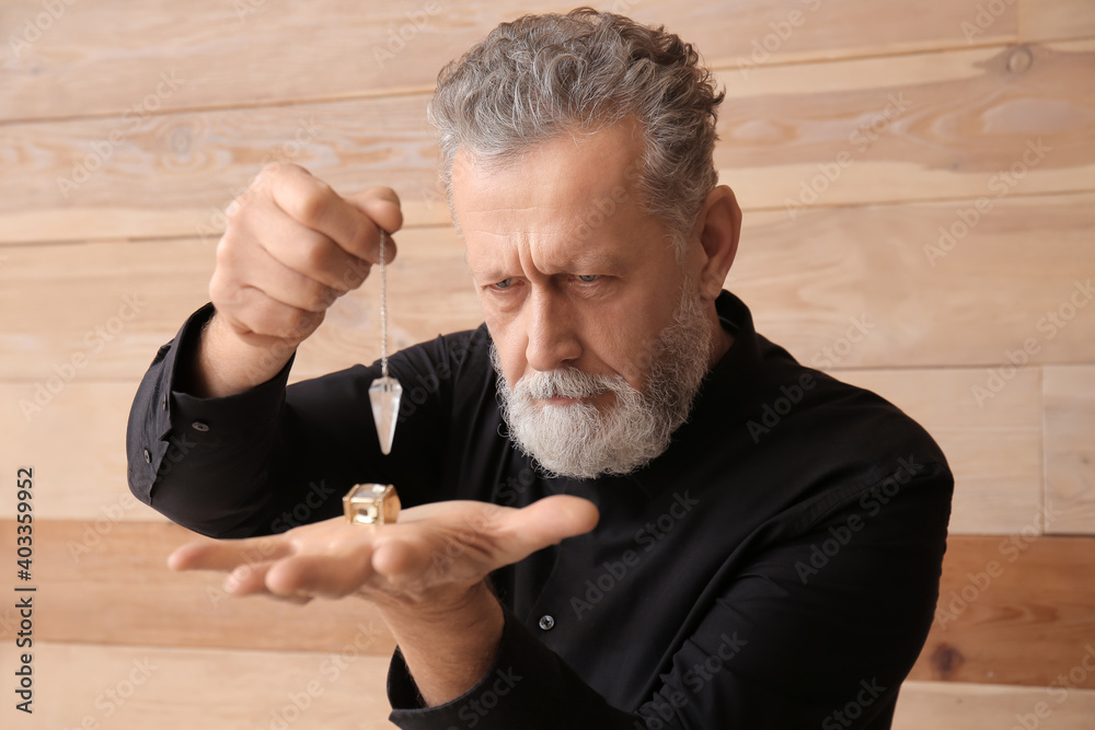 Male fortune teller with pendulum on wooden background