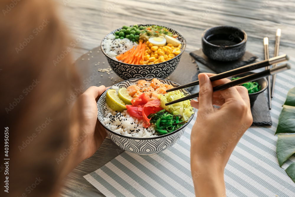 Woman eating tasty rice poke bowl