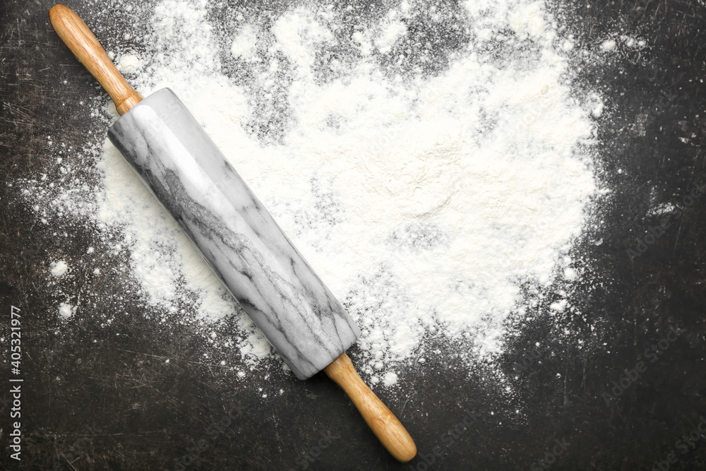 Marble rolling pin and flour on dark background