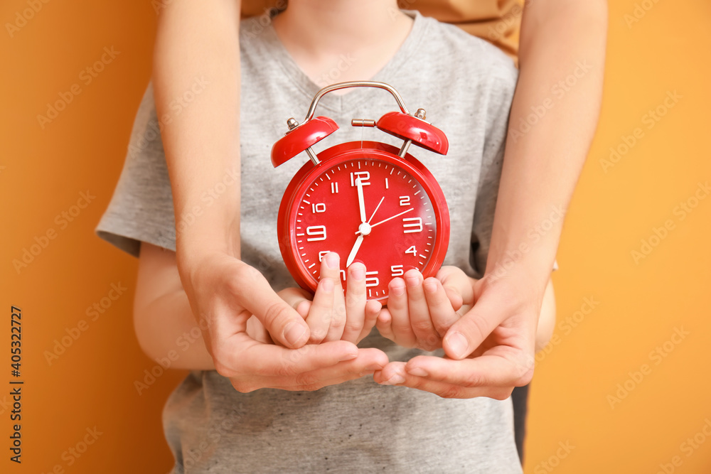 Hands of family with alarm clock on color background