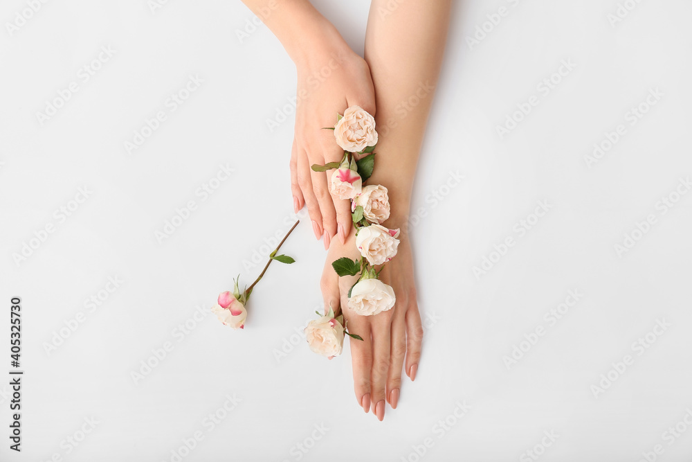 Female hands with beautiful flowers on light background