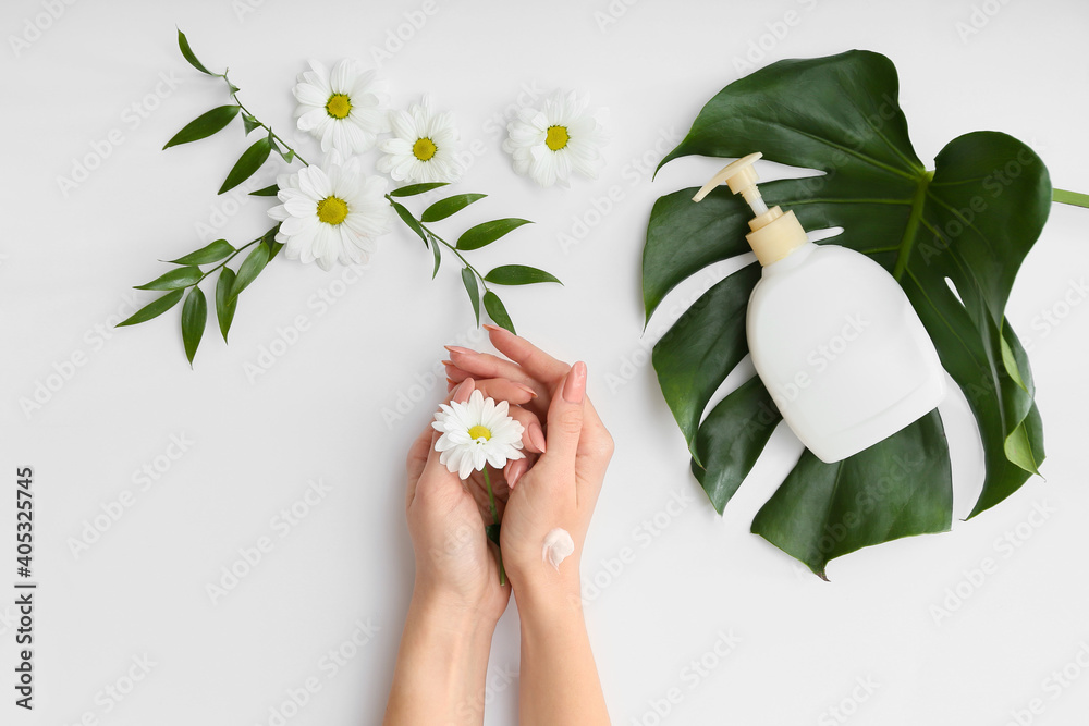 Female hands with cream, tropical leaf and beautiful flowers on light background