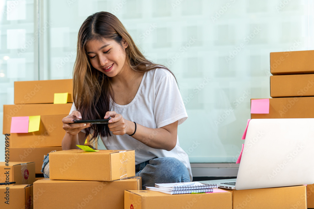 The Asian owner takes pictures of a brown package to verify his customers address and make arrangem