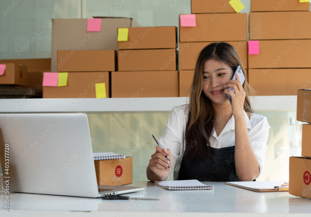 Young Asian entrepreneur owner talking on phone at workplace at home. Start up small business.