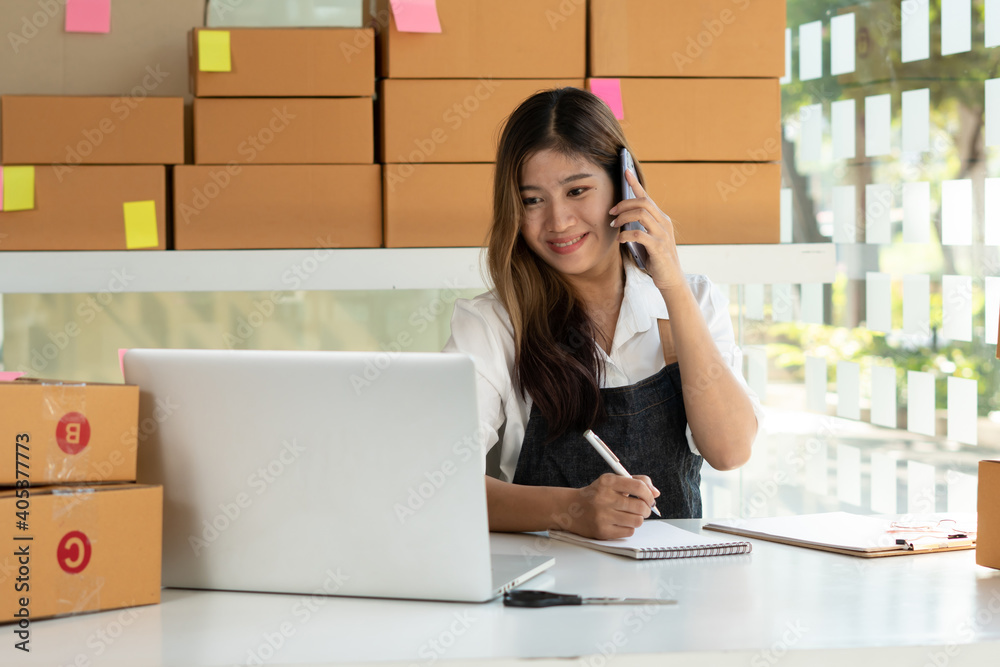 Young Asian entrepreneur owner talking on phone at workplace at home. Start up small business.