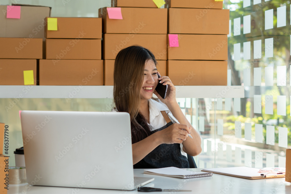 Young Asian entrepreneur owner talking on phone at workplace at home. Start up small business.