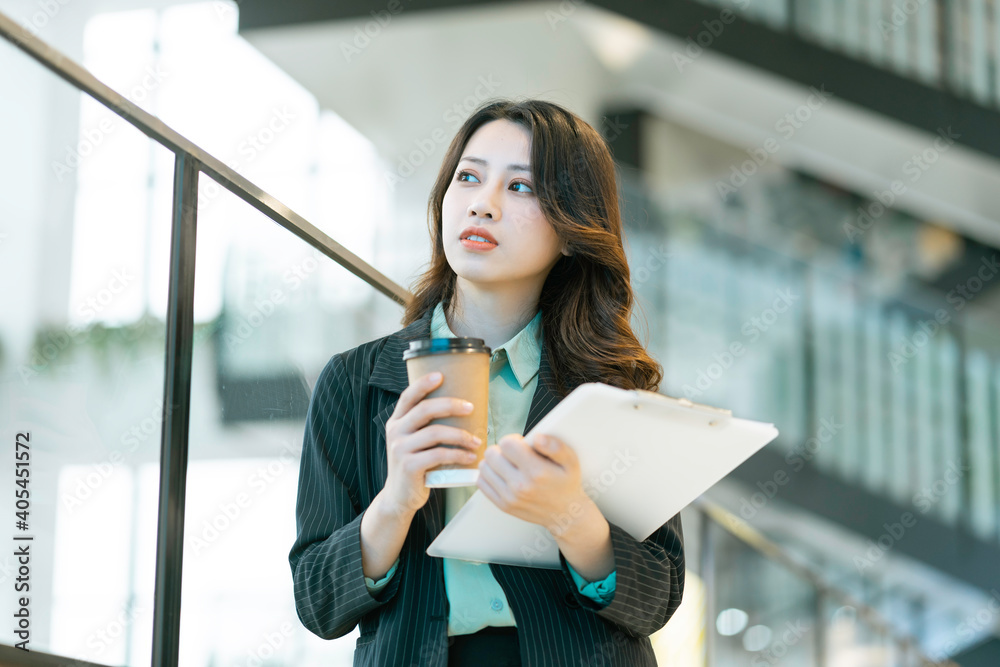 Young Asian businesswoman standing holding documents and coffee cup