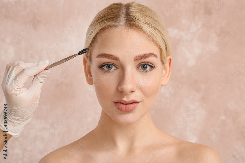 Young woman undergoing eyebrow correction procedure on color background