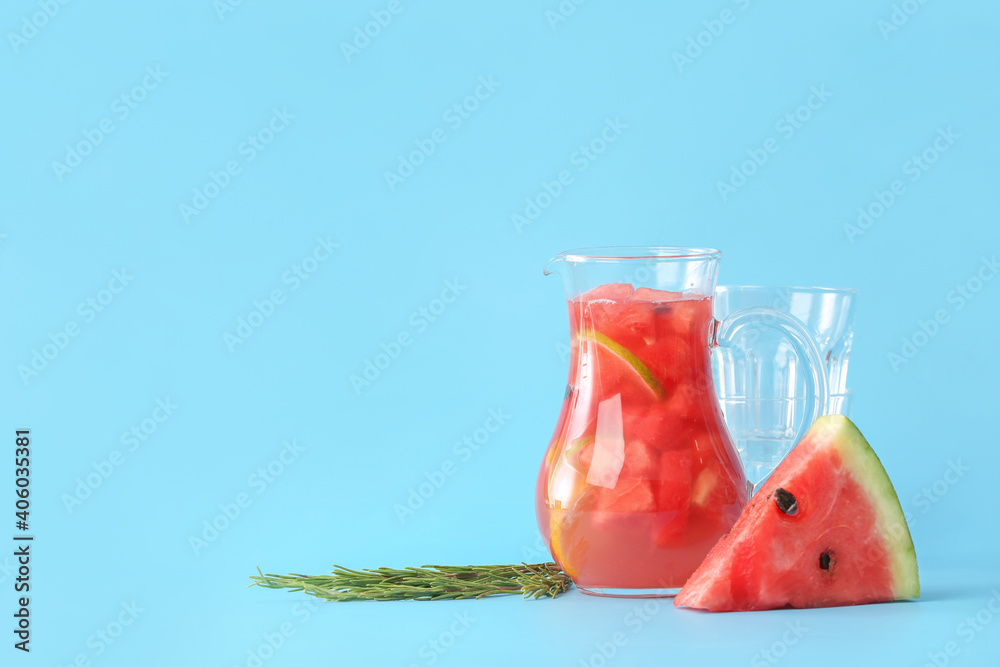 Jug of cold watermelon lemonade and glasses on color background