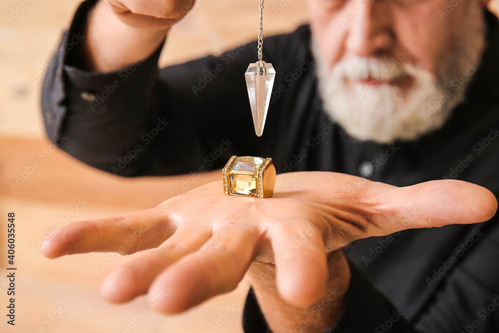 Male fortune teller with pendulum on wooden background, closeup