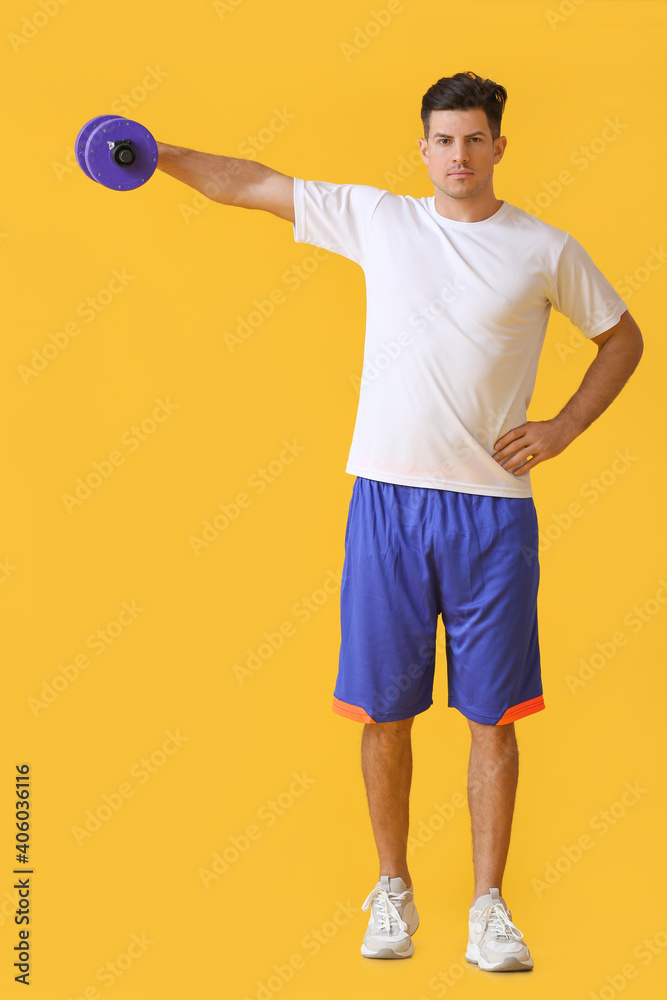 Sporty young man training with dumbbell on color background