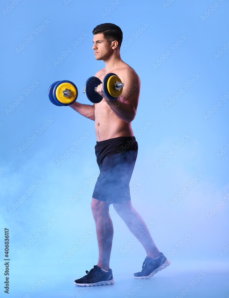 Sporty young man training with dumbbells on color background