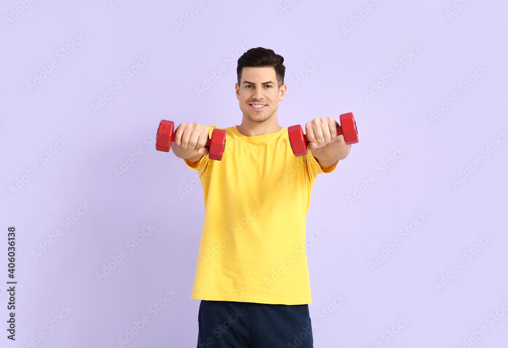 Sporty young man training with dumbbells on color background