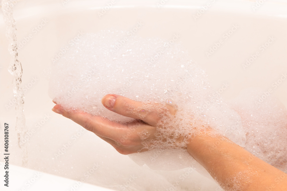 soap foam forms on a womans hand in the bathroom, a stream of water. background light tile