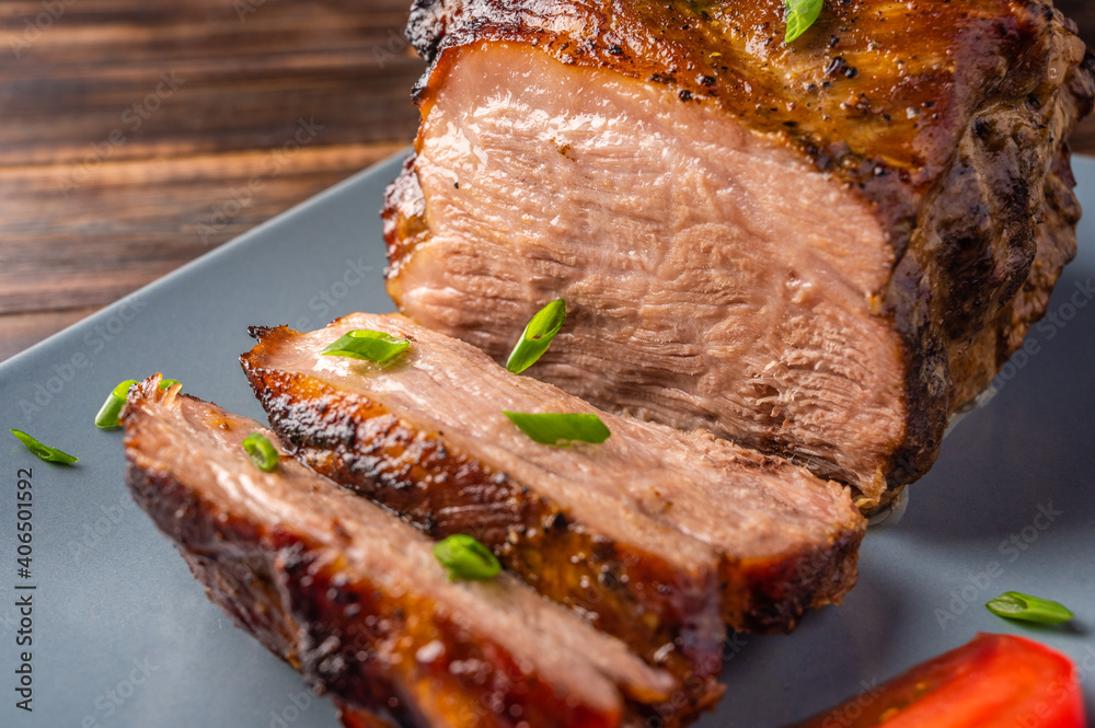 Piece of slow cooked oven-pulled pork shoulder on plate with green onion and tomato, close-up. Selec