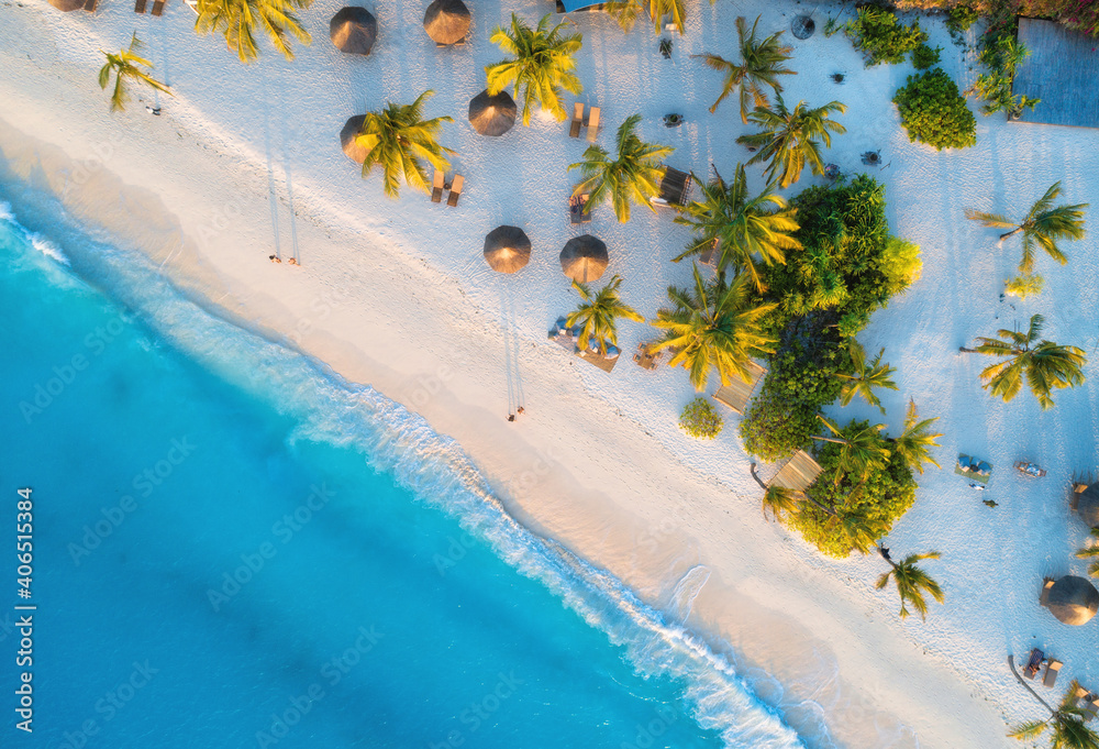 Aerial view of umbrellas, palms on the sandy beach of Indian Ocean at sunset. Summer in Zanzibar, Af