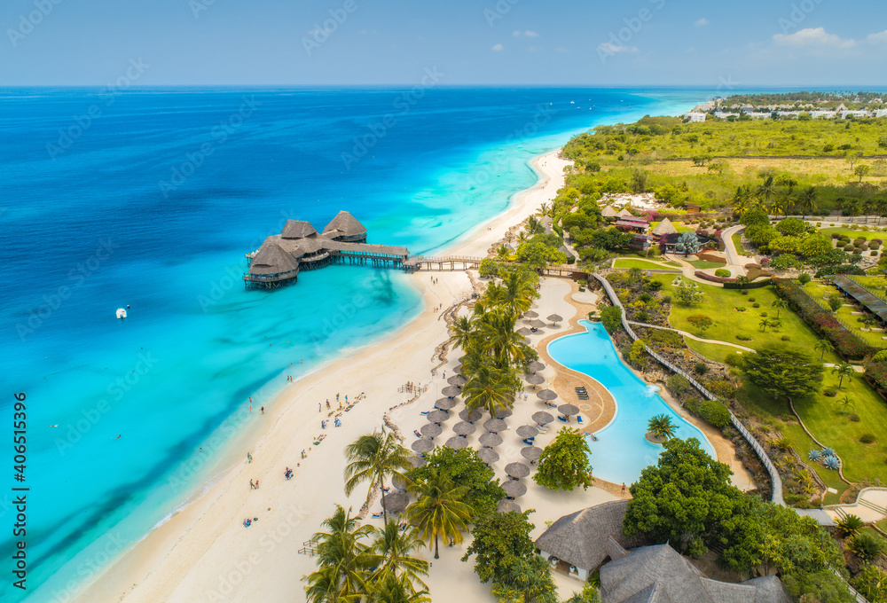 Aerial view of beautiful hotel on the sea, pool, umbrellas and green palm trees on the sandy beach a