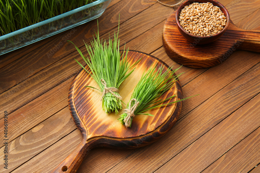 Fresh wheatgrass and seeds in bowl on wooden background