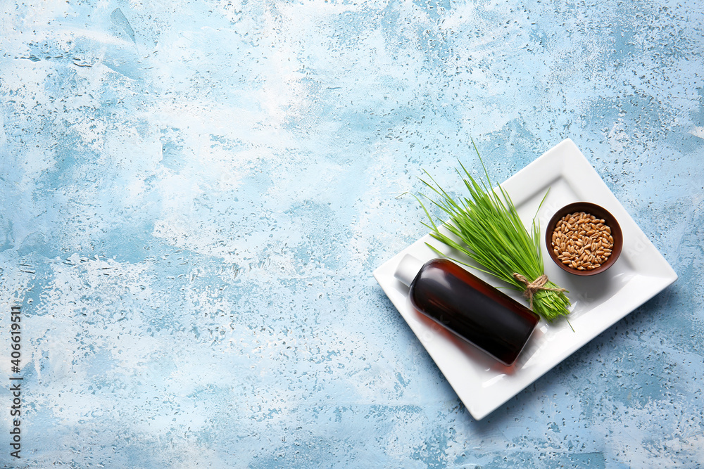 Fresh wheatgrass, seeds in bowl and bottle on color background