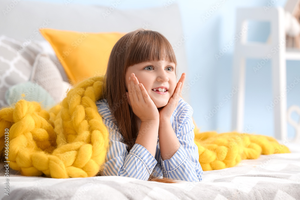 Happy little girl with warm plaid lying on bed at home