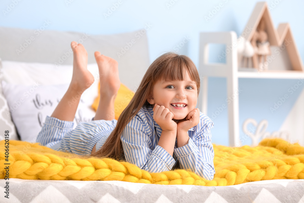 Happy little girl with warm plaid lying on bed at home