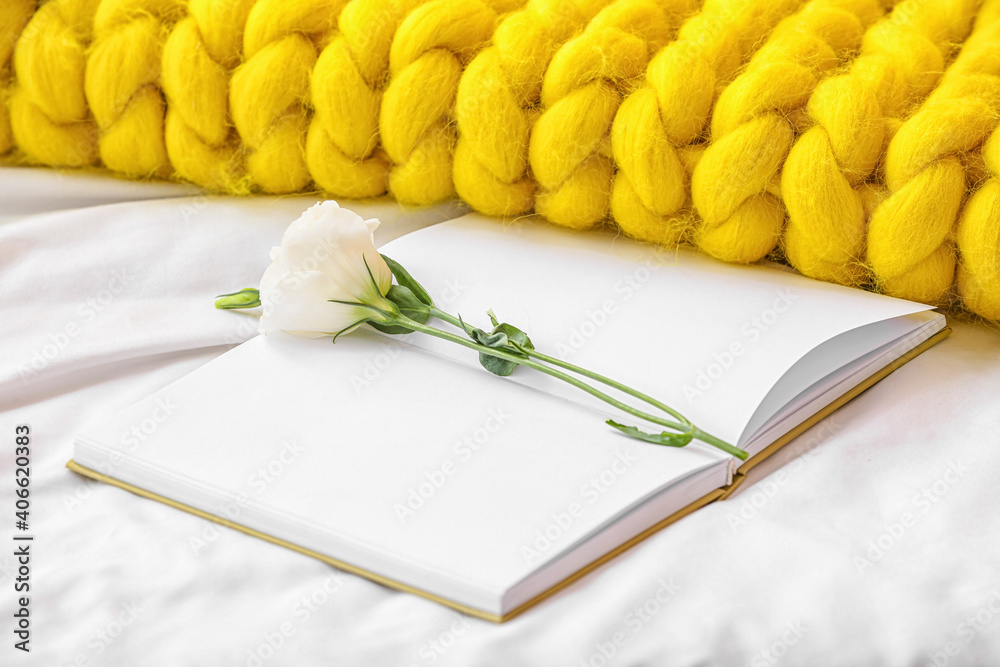 Book with flower and knitted plaid on bed