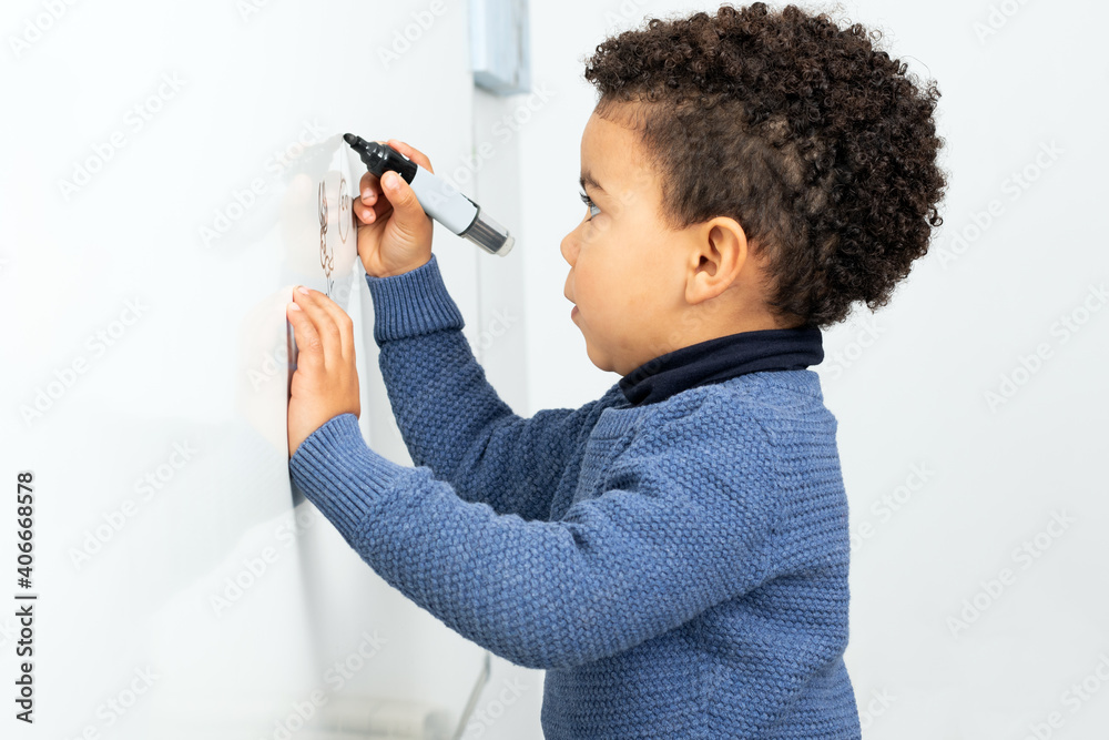 Cute afro american boy drawing on white board.