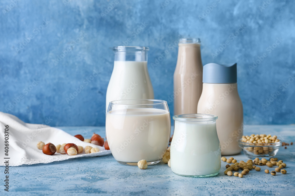 Bottles and glass of different vegan milk on color background