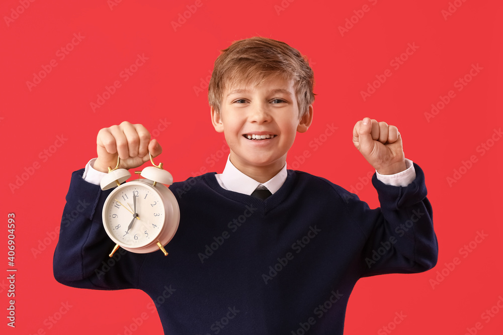 Happy little schoolboy with alarm clock on color background