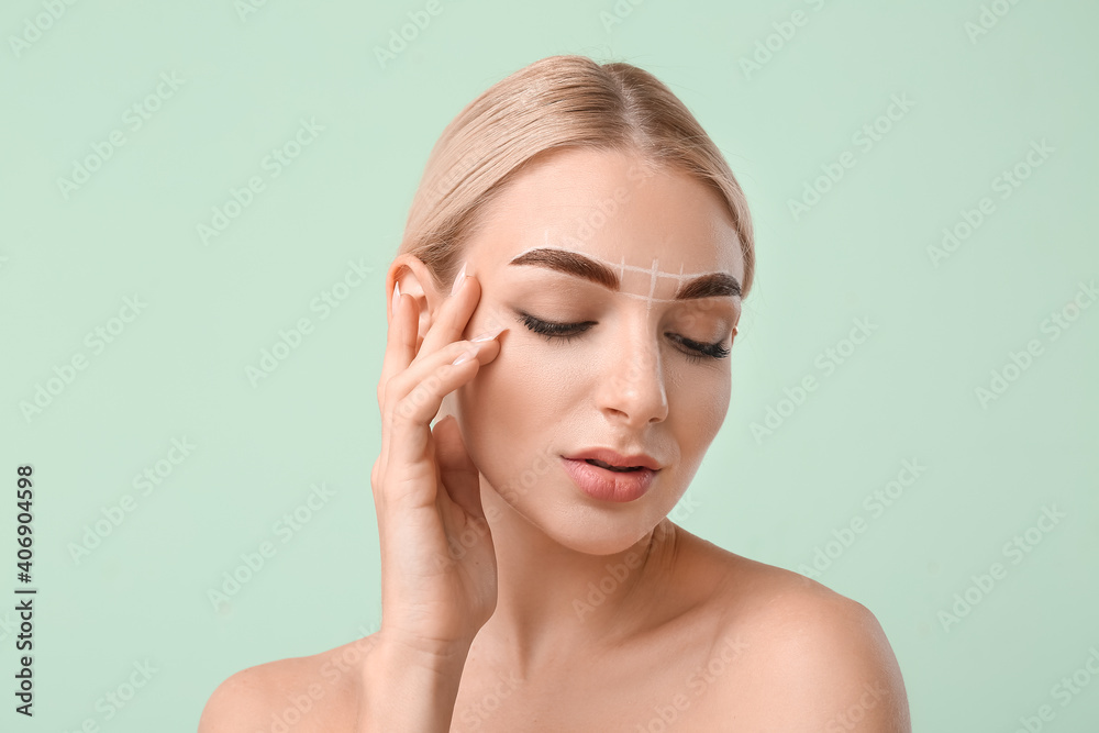 Young woman with marking for eyebrow correction on color background