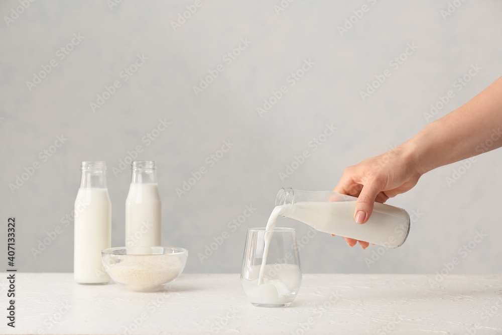 Woman pouring rice milk from bottle into glass on table