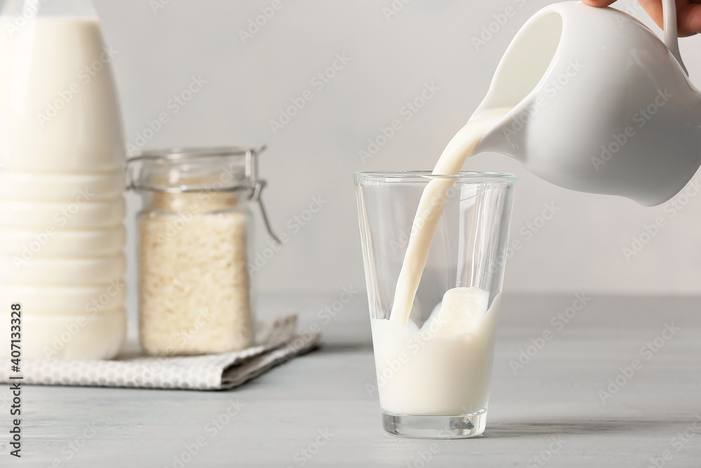 Pouring of rice milk from jug into glass on table