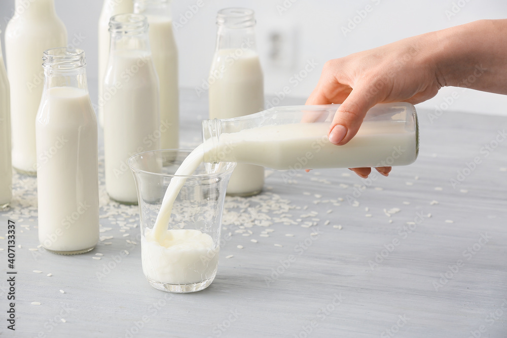 Woman pouring rice milk from bottle into glass on table