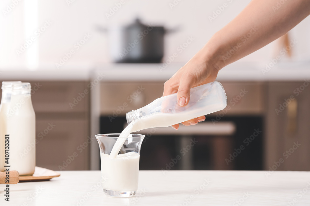 Woman pouring rice milk from bottle into glass on table